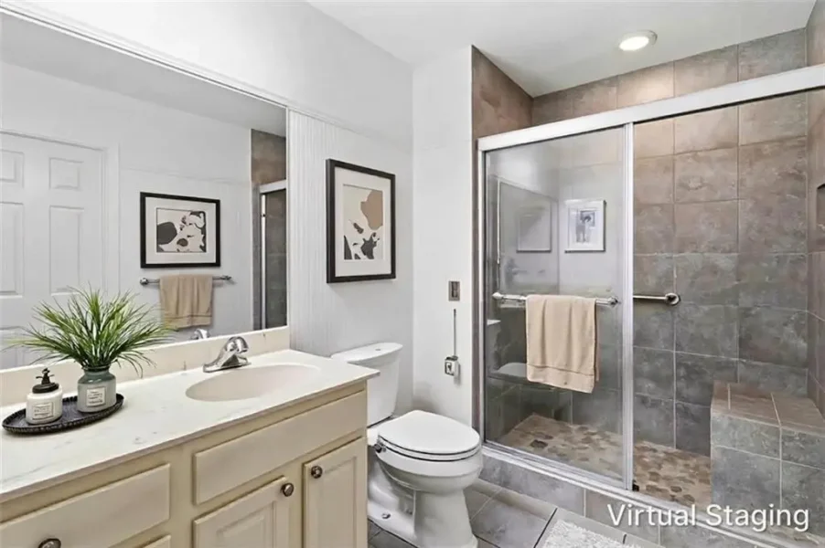 Bright bathroom with cream vanity, single sink, and large mirror; toilet beside a glass-door shower with beige tiles and towel bar clearly visible.