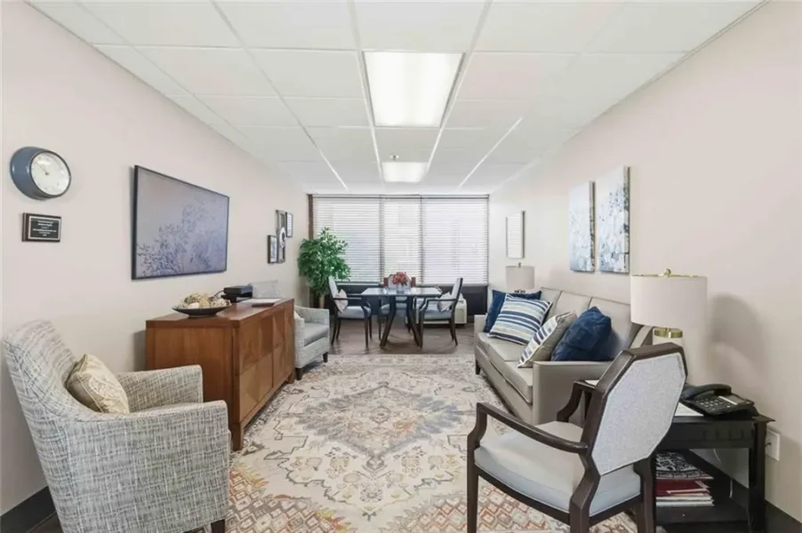 Cozy office waiting area with sofa, armchairs, a coffee table, and a patterned rug by a window.