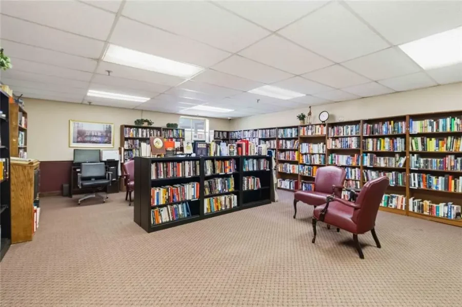 Cozy library reading area with tall bookshelves, burgundy armchairs, and a carpeted floor lens.